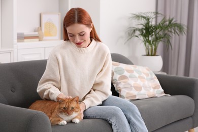 Woman stroking her cute cat on sofa at home