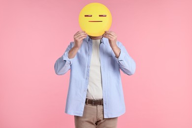 Photo of Man holding emoticon with closed eyes and mouth on pink background