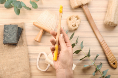 Woman holding natural bamboo toothbrush over table with bath items, top view