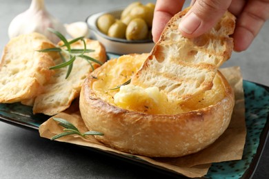 Woman dipping bread into baked brie cheese at grey table, closeup