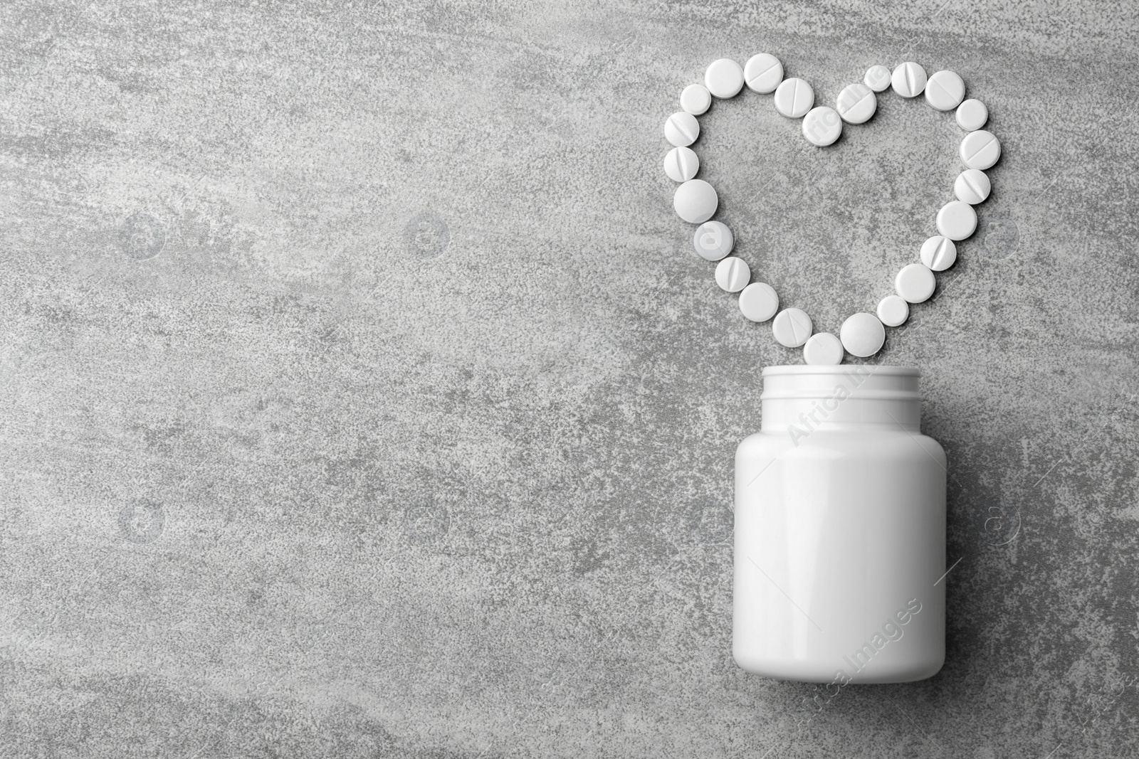 Photo of Bottle and heart of pills on grey background, flat lay. Space for text