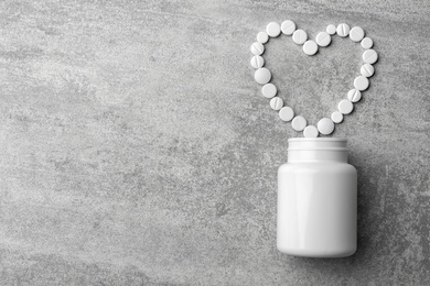 Photo of Bottle and heart of pills on grey background, flat lay. Space for text