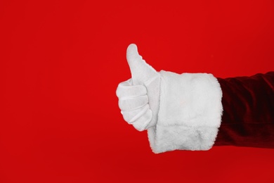 Photo of Santa Claus showing thumb up on red background, closeup of hand