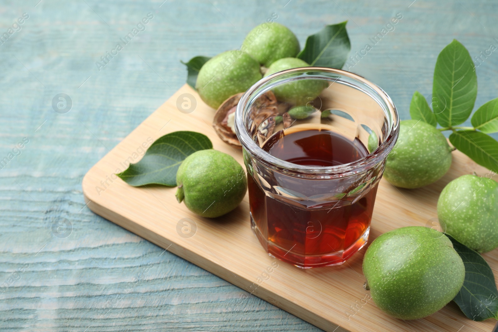 Photo of Delicious liqueur and green walnuts on light blue wooden table