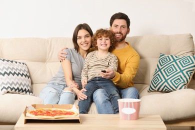 Happy family watching TV with popcorn and pizza on sofa