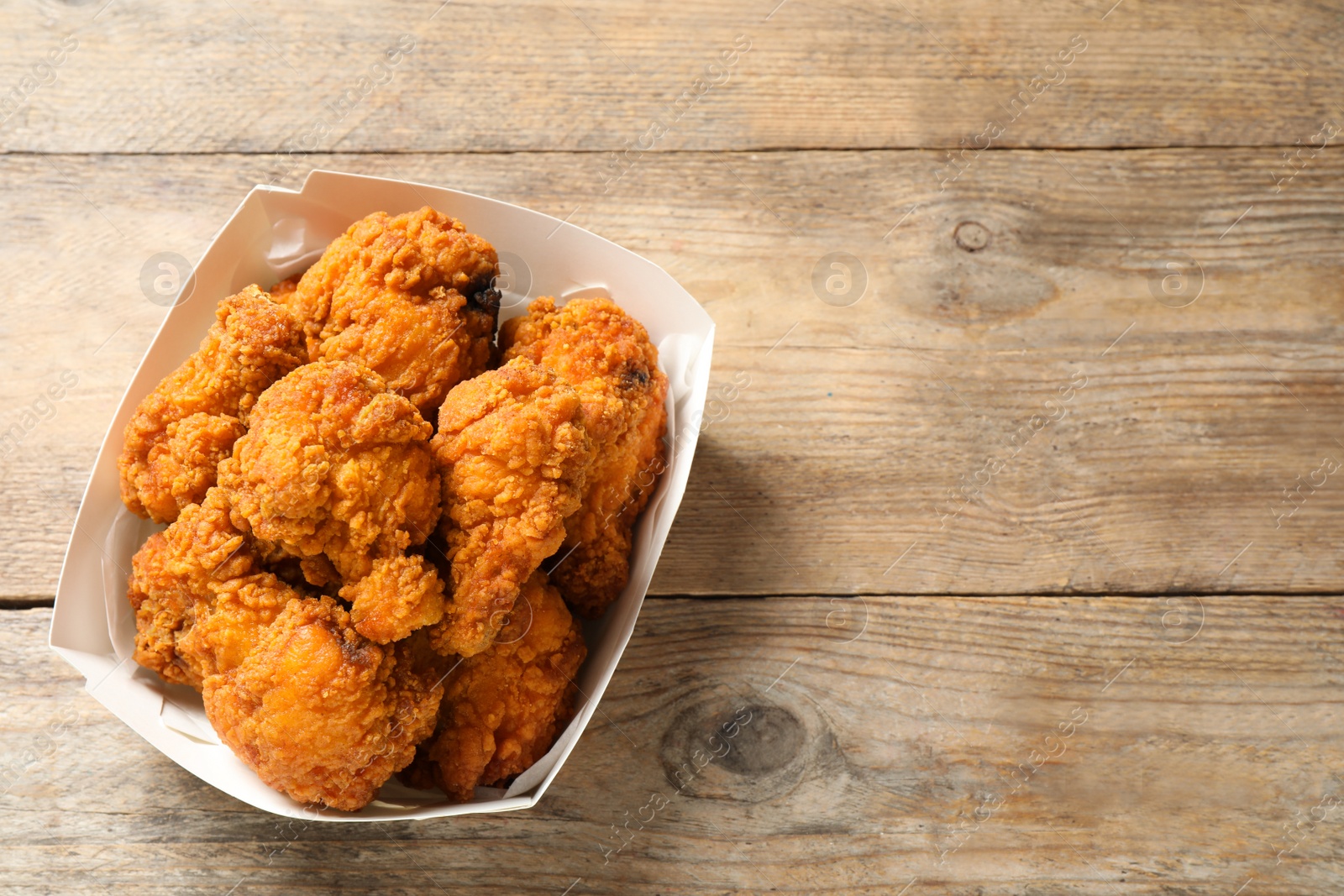 Photo of Tasty deep fried chicken pieces on wooden table, top view. Space for text