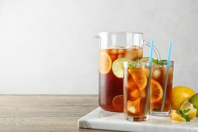Photo of Glasses and jug of refreshing iced tea on wooden table against light background. Space for text