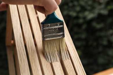 Photo of Man applying varnish onto wooden crate against blurred background, closeup. Space for text
