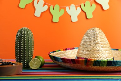 Photo of Mexican sombrero hat, decorative cactus and lime on color table, closeup