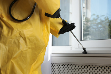 Pest control worker spraying pesticide on window sill indoors, closeup