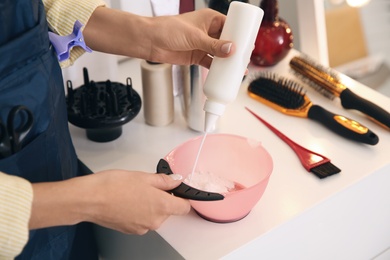 Professional hairdresser preparing dye for hair coloring at white table in beauty salon, closeup