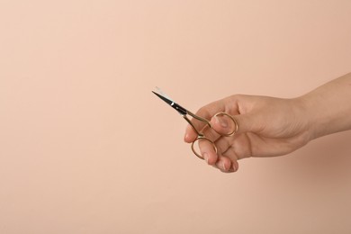 Photo of Woman holding sewing scissors on beige background, closeup. Space for text