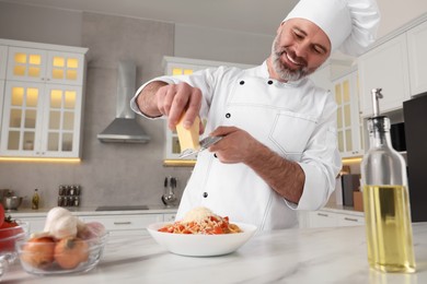 Photo of Professional chef grating cheese into delicious dish at white marble table in kitchen, low angle view