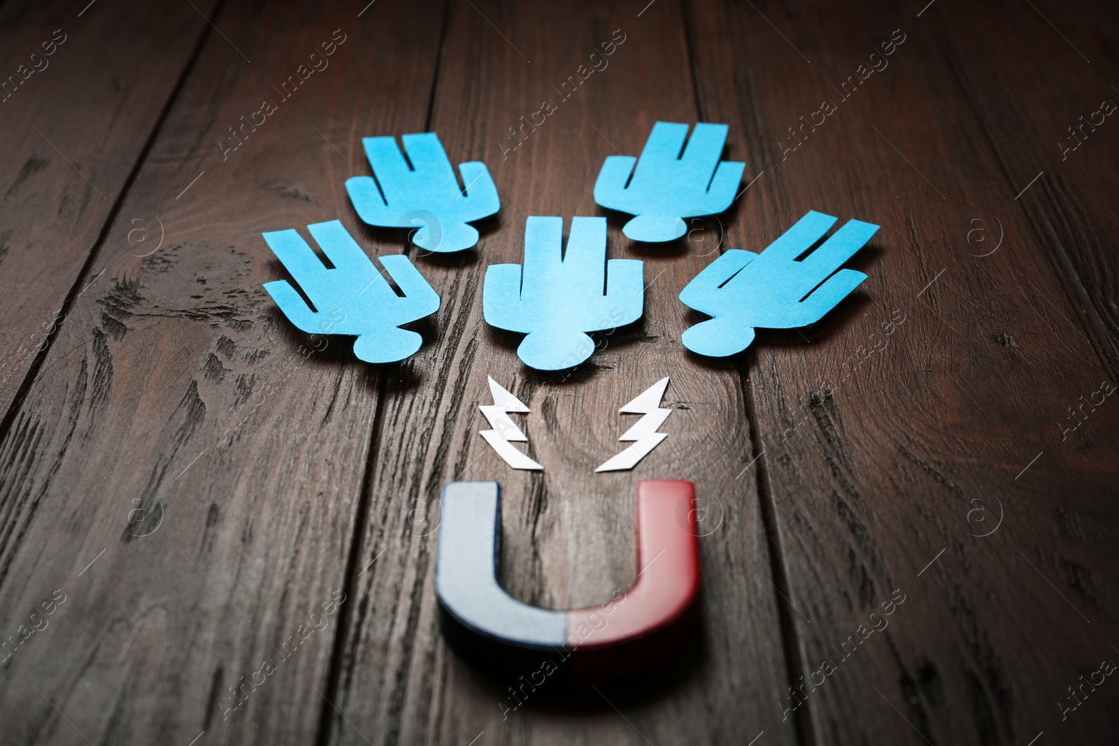 Photo of Magnet attracting paper people on wooden background