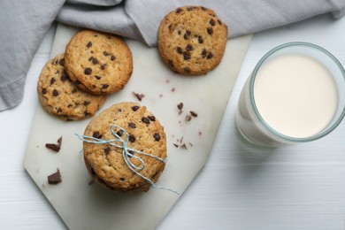 Photo of Tasty chocolate chip cookies and glass of milk on white wooden table, flat lay