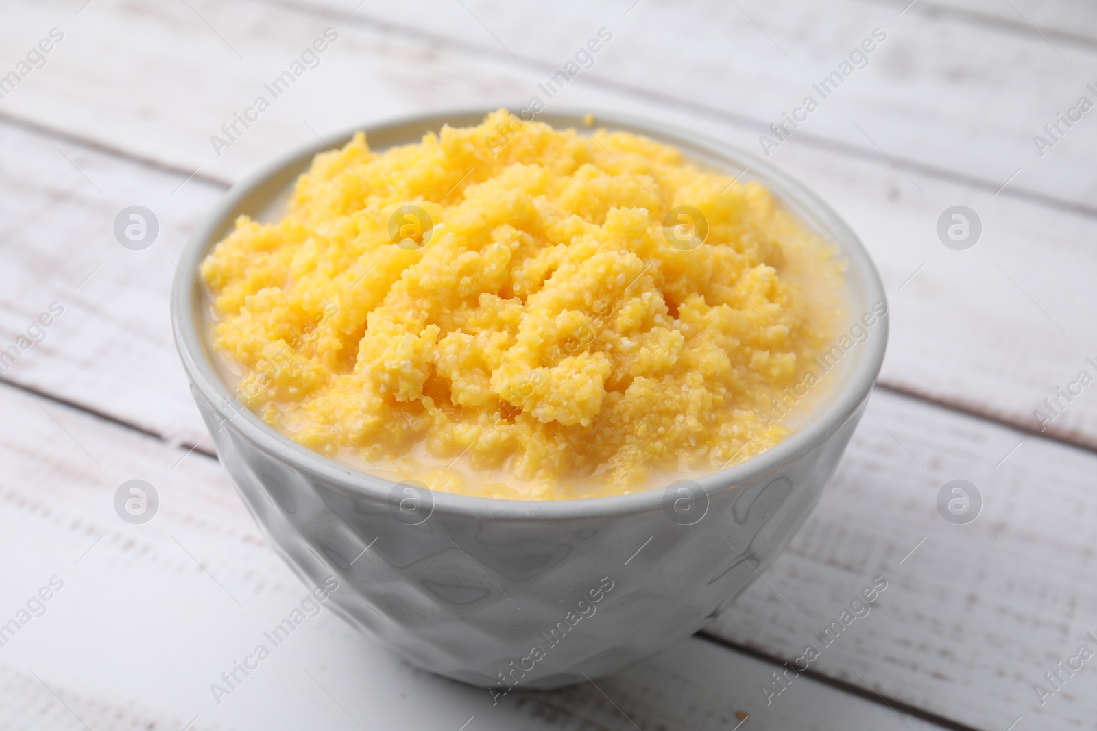 Photo of Tasty cornmeal in bowl on white wooden table, closeup