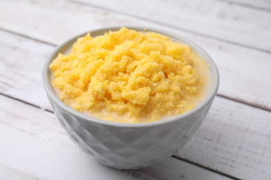 Photo of Tasty cornmeal in bowl on white wooden table, closeup