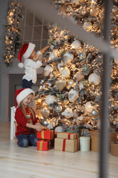 Cute little children near Christmas tree in living room, view through window