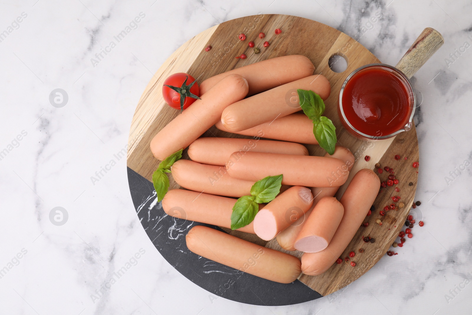 Photo of Delicious boiled sausages with spices, sauce and tomato on white marble table, top view