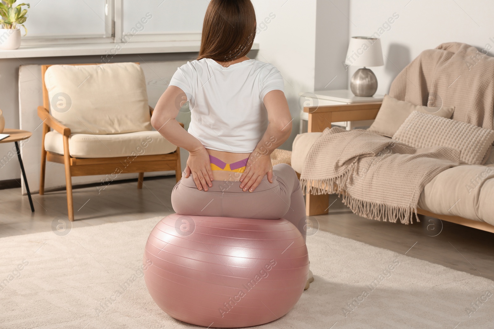 Photo of Pregnant woman with kinesio tapes doing exercises on fitball at home, back view