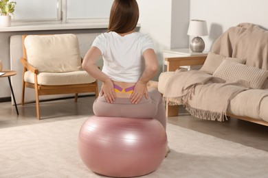 Photo of Pregnant woman with kinesio tapes doing exercises on fitball at home, back view