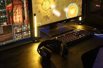 Playing video games. Computer monitor, keyboard, mouse and headphones on table indoors