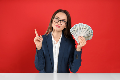 Young woman with money at table on crimson background