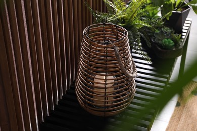 Photo of Stylish wicker holder with burning candle and beautiful houseplant on bench near wood slat wall