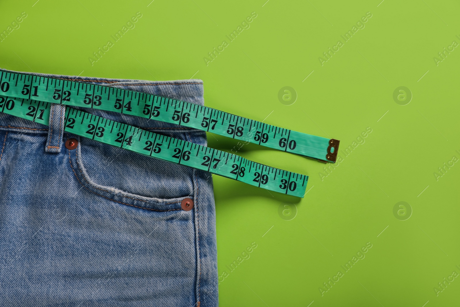 Photo of Jeans and measuring tape on light green background, top view with space for text. Weight loss concept