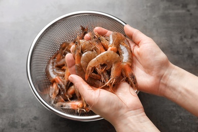 Woman holding fresh shrimps over colander, closeup