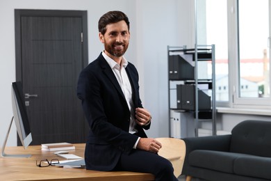 Photo of Smiling bearded man sitting on table in office