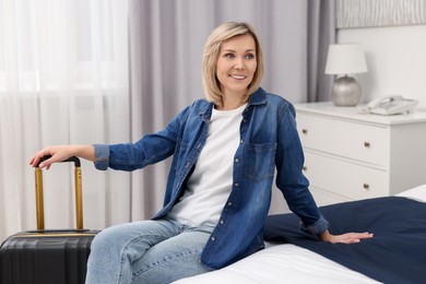 Smiling guest with suitcase relaxing on bed in stylish hotel room