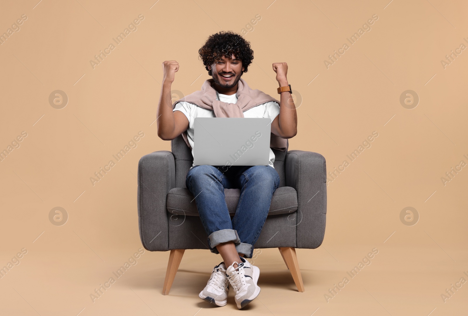 Photo of Happy man with laptop sitting in armchair on beige background