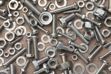 Photo of Different metal bolts and nuts on beige textured table, flat lay