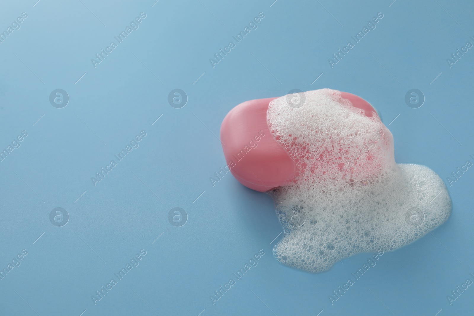 Photo of Soap bar with fluffy foam on light blue background, space for text