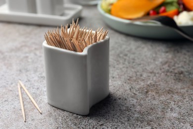 Photo of Holder with many bamboo toothpicks on grey table, closeup. Space for text