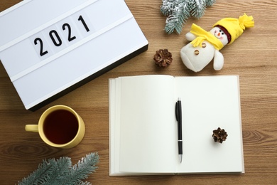 Photo of Light box with number 2021 near notebook, new year goals. Flat lay composition on wooden table