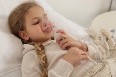 Photo of Little girl using nebulizer for inhalation on bed indoors