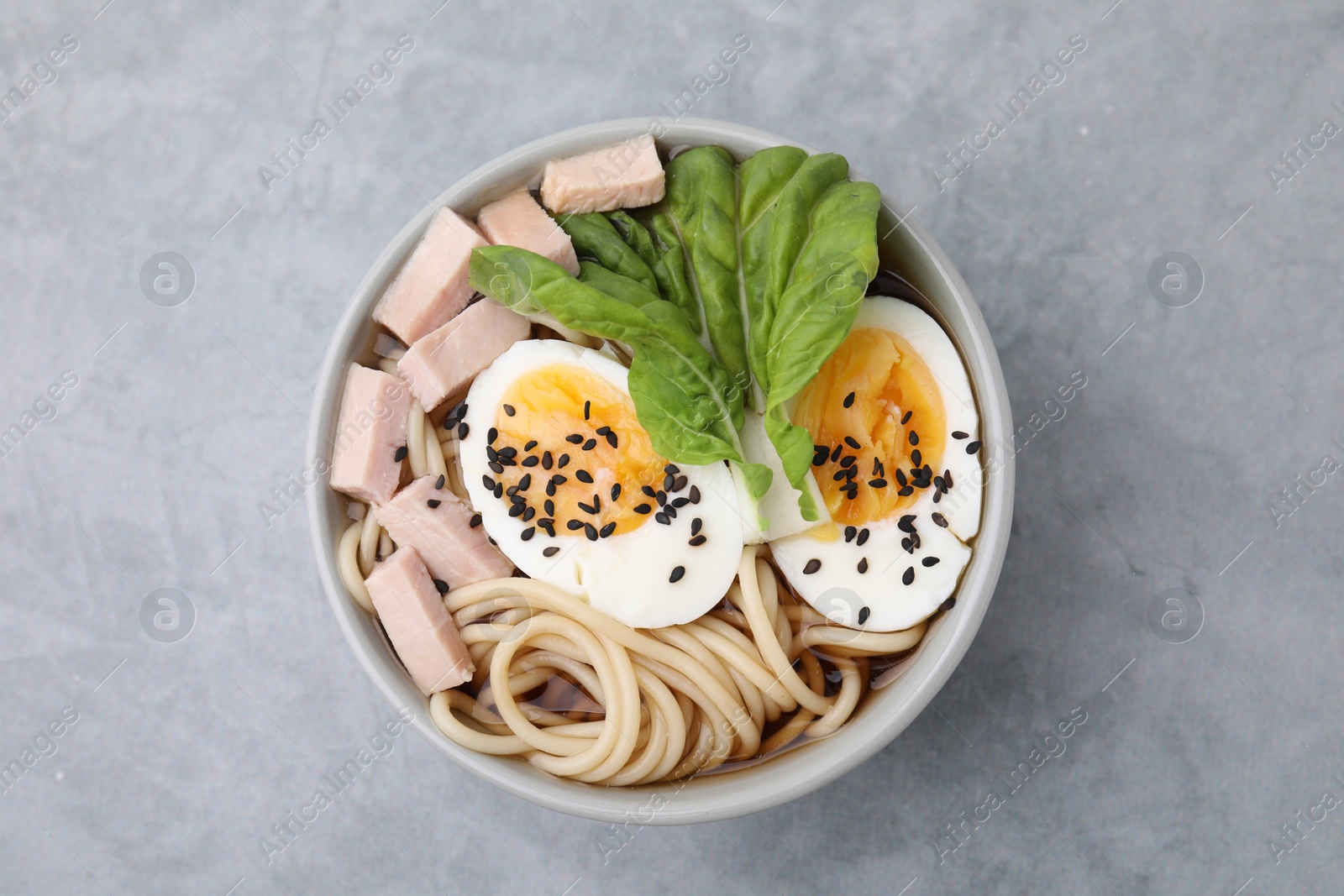 Photo of Bowl of delicious ramen with meat and egg on light grey table, top view. Noodle soup