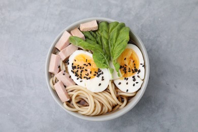 Photo of Bowl of delicious ramen with meat and egg on light grey table, top view. Noodle soup