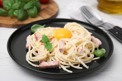 Photo of Plate of tasty pasta Carbonara with basil leaves and egg yolk on white textured table, closeup