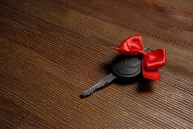 Photo of Key with red bow on wooden background, space for text. Car buying