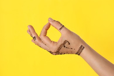 Photo of Woman with henna tattoo on hand against yellow background, closeup. Traditional mehndi ornament