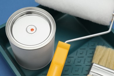 Photo of Can of orange paint, brush, roller and container on blue background, closeup