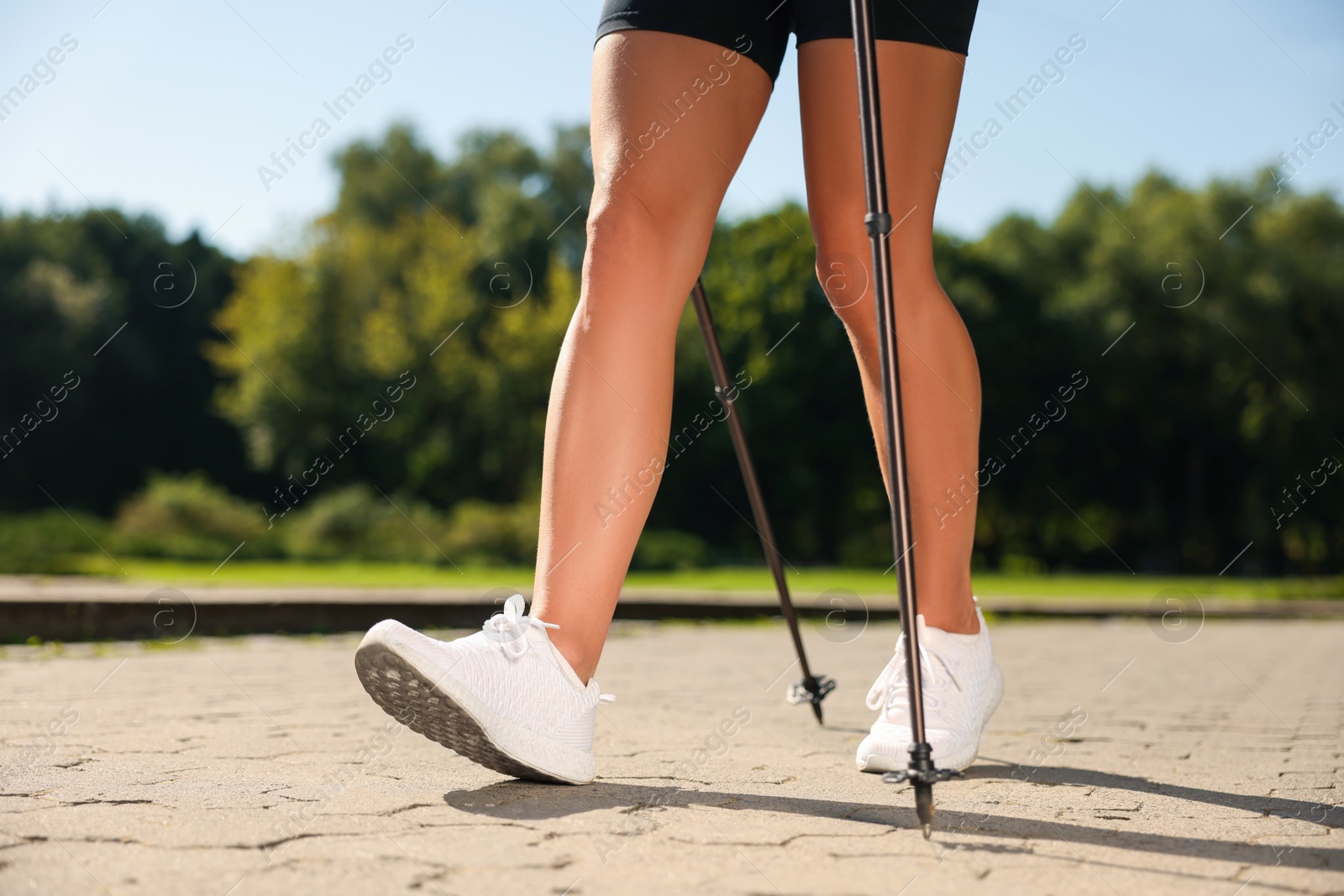 Photo of Woman practicing Nordic walking with poles outdoors on sunny day, closeup