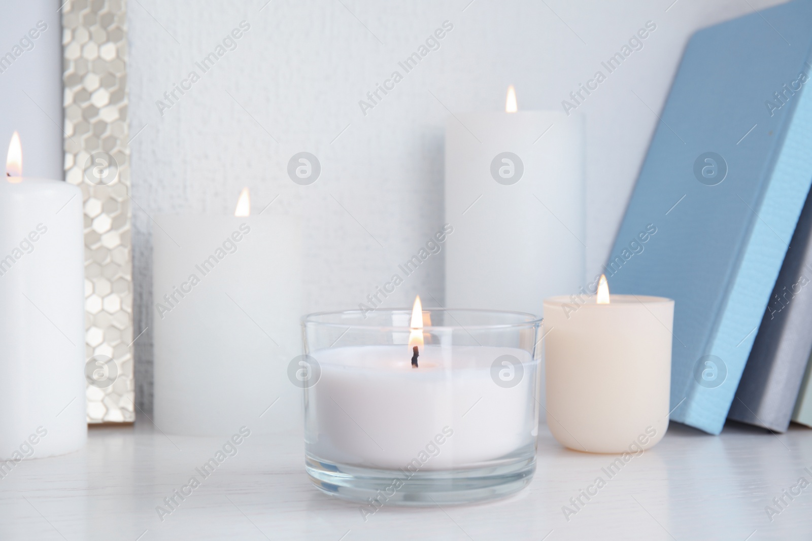 Photo of Burning aromatic candles in holders on bookshelf