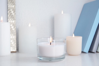 Burning aromatic candles in holders on bookshelf