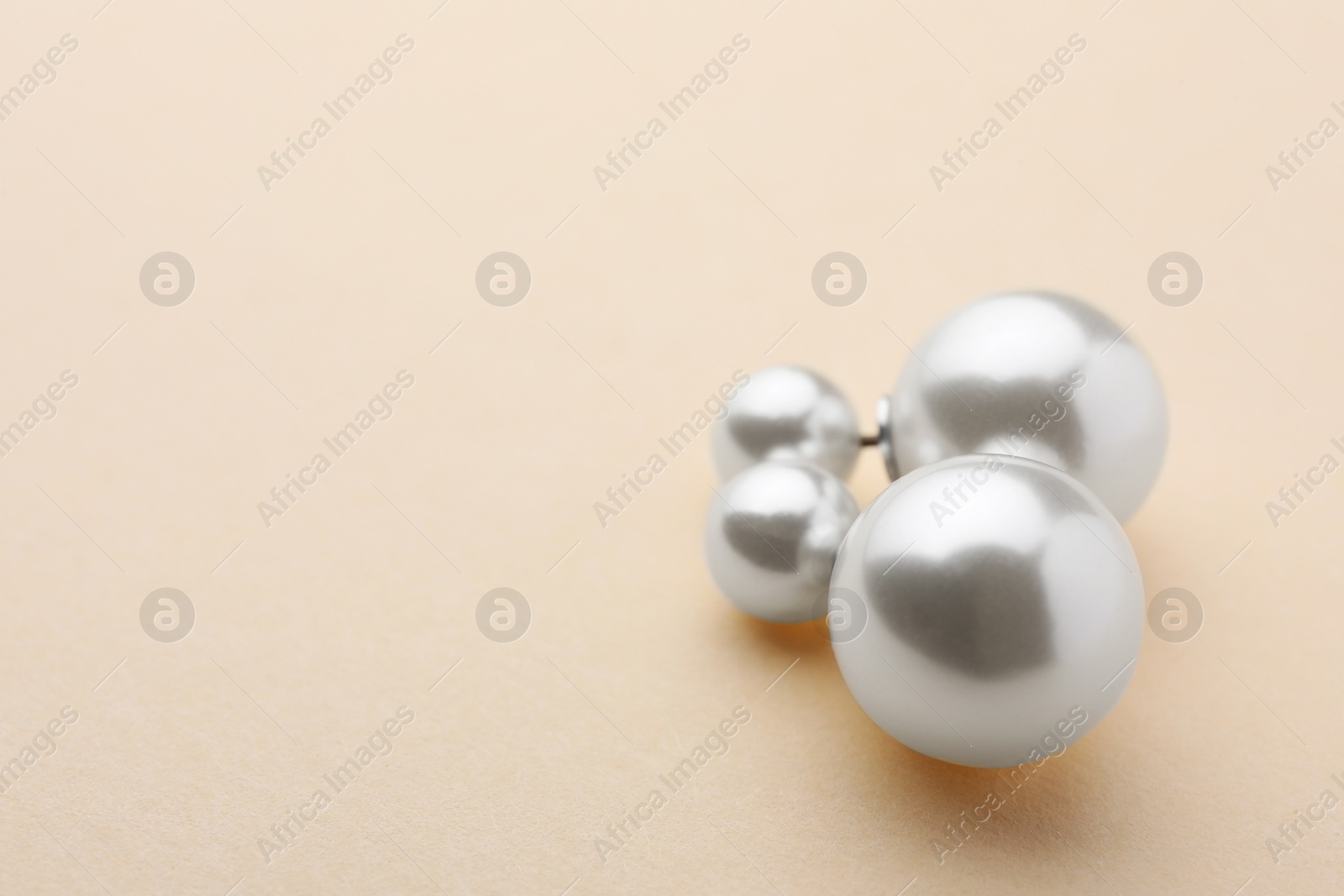 Photo of Elegant earrings with pearls on beige background. Space for text