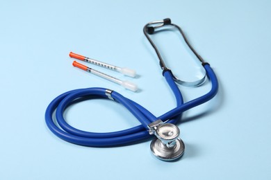 Photo of Stethoscope and syringes on light blue background, closeup. Medical tools