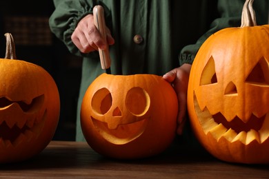 Woman carving pumpkin for Halloween at wooden table, closeup